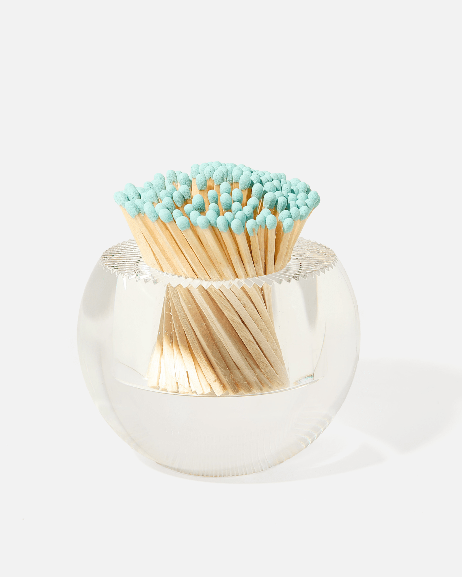 The Acrylic Match Striker Collection by Tart by Taylor holds a bundle of wooden matches with light blue tips, arranged heads up in a round glass container with an acrylic match strike—a stylish coffee table accessory.