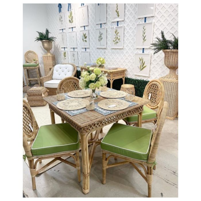 A dining area featuring Mainly Baskets Home's Trellis Game Table and four chairs with green cushions, styled with placemats, flowers, coordinating wicker furniture, botanical wall art, and sophisticated accents.
