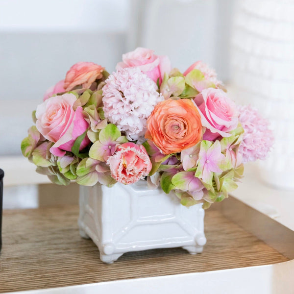 A vibrant bouquet of pink roses and the Live Mother's Day Floral Arrangement in a white ceramic vase on a wooden table by Hive Floral Studio.