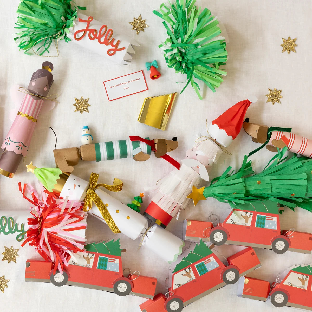 Meri Meri Santa, Reindeer & Tree Crackers shaped like Santa, reindeer, and cars, accompanied by an elf joke card and scattered gold star confetti.