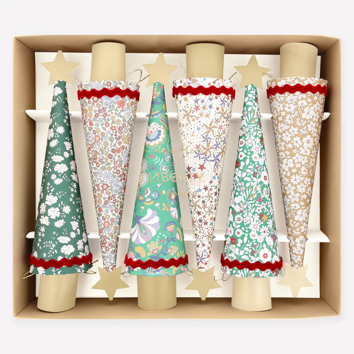 Meri Meri Liberty Tree Crackers: six tree-shaped party crackers in various floral and star-patterned paper designs, each topped with a gold star, arranged in a cardboard tray.
