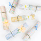 Seven Meri Meri Flower Crackers, adorned with artificial flowers, ribbons, and a charming enamel pin party favor, are displayed on a white background.