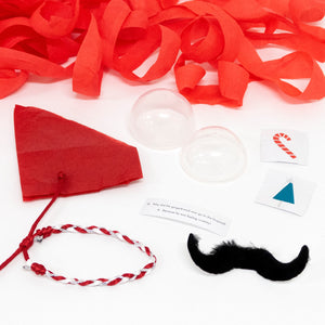 Peppermint Candy Surprise Balls by Meri Meri include red streamers, a red paper hat, plastic domes, a braided bracelet, fake mustache, printed cards, and a joke—perfect festive treats or stocking fillers for party bags. All displayed on a white surface.