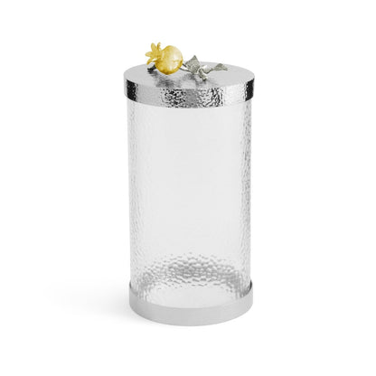 The Michael Aram Pomegranate Silver & Gold Canister is a cylindrical glass canister with a textured surface and a silver lid, topped with a gold pomegranate and silver leaves—symbols of abundance.