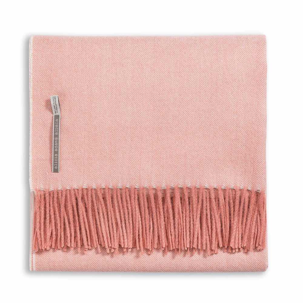 The Classic Herringbone Throw Collection by Alicia Adams Alpaca features a pink wool throw with fringe, crafted from baby alpaca wool in Peru. Fair-trade and elegant, it adds warmth and style to any space.