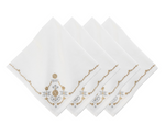 Four napkins from the Juliska Heidi Gold/Silver Embroidered Napkin Set are arranged in a fanned stack. Each white linen-blend napkin is embroidered with gold and gray floral and scroll designs, accented by an Alpine motif in one corner.