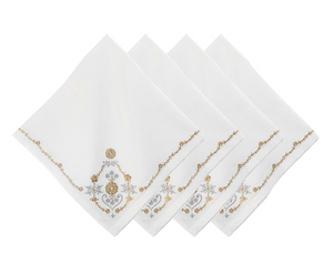 Four napkins from the Juliska Heidi Gold/Silver Embroidered Napkin Set are arranged in a fanned stack. Each white linen-blend napkin is embroidered with gold and gray floral and scroll designs, accented by an Alpine motif in one corner.