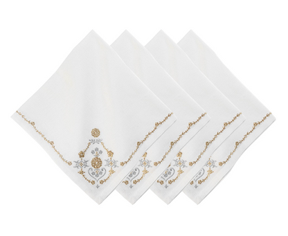 Four napkins from the Juliska Heidi Gold/Silver Embroidered Napkin Set are arranged in a fanned stack. Each white linen-blend napkin is embroidered with gold and gray floral and scroll designs, accented by an Alpine motif in one corner.
