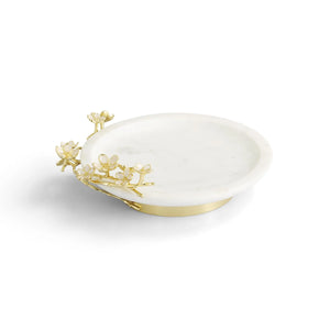From the Cherry Blossom Collection by Michael Aram, a round white marble dish features gold floral accents inspired by Japanese motifs, displayed on a plain white background.