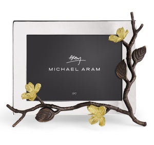 The Michael Aram Dogwood Frame is a handcrafted goldtone photo frame featuring a bronze and gold branch with dogwood leaves and flowers on the right, adding elegance to your décor.