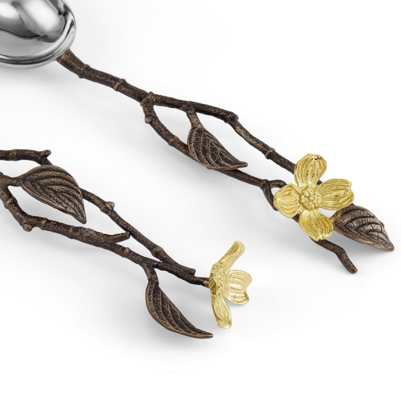 A close-up of two ornate utensils from the Michael Aram Dogwood Serveware Collection, highlighting nature-inspired branch handles decorated with gold-toned flowers and leaves.