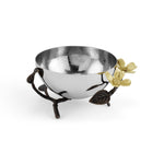 A shiny silver bowl rests in a decorative stand with branch-like supports, bronze leaves, and gold-toned flowers—showcasing the nature-inspired Dogwood Serveware Collection by Michael Aram.