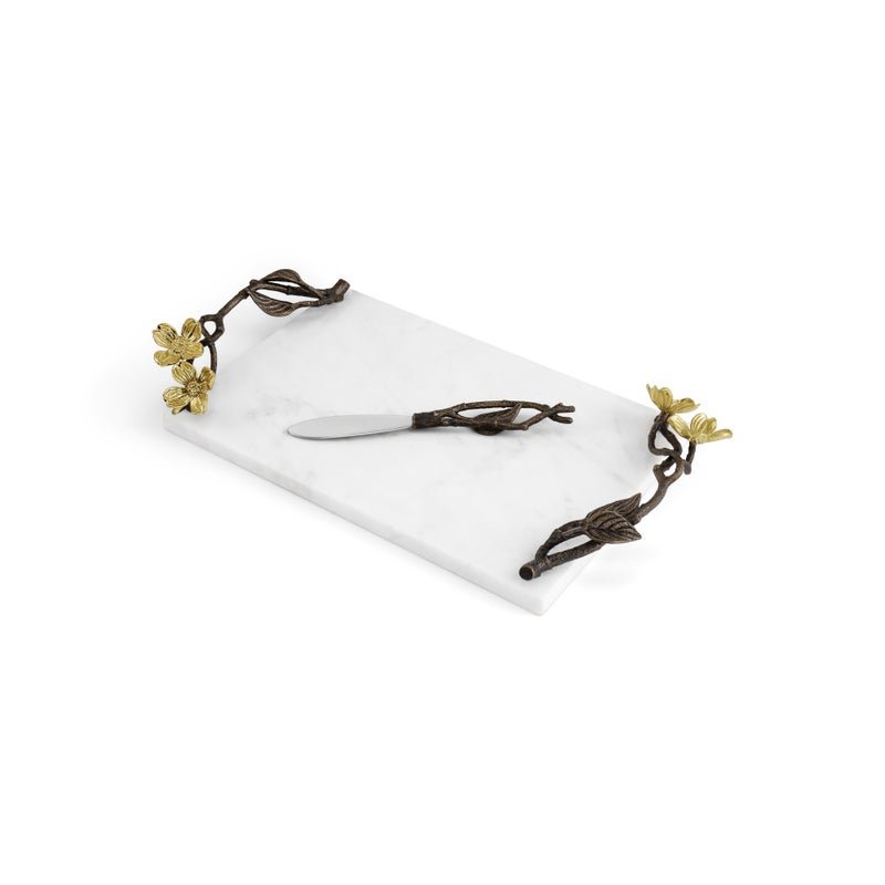 A rectangular white marble serving board with gold-tone dogwood metal handles and a silver spreader knife from Michael Aram’s Dogwood Serveware Collection—an elegant, nature-inspired design.