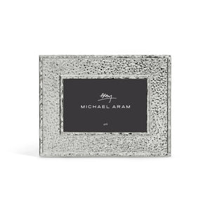 The Hammertone Frame by Michael Aram is a silver, textured rectangular photo frame featuring a refined hammertone metal finish and a black inner label displaying the “Michael Aram” signature in white text, designed to hold a 4x6 photo.