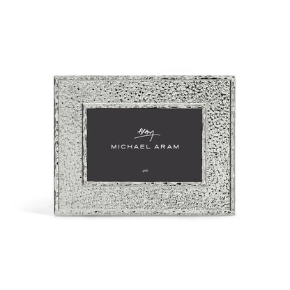 The Hammertone Frame by Michael Aram is a silver, textured rectangular photo frame featuring a refined hammertone metal finish and a black inner label displaying the “Michael Aram” signature in white text, designed to hold a 4x6 photo.