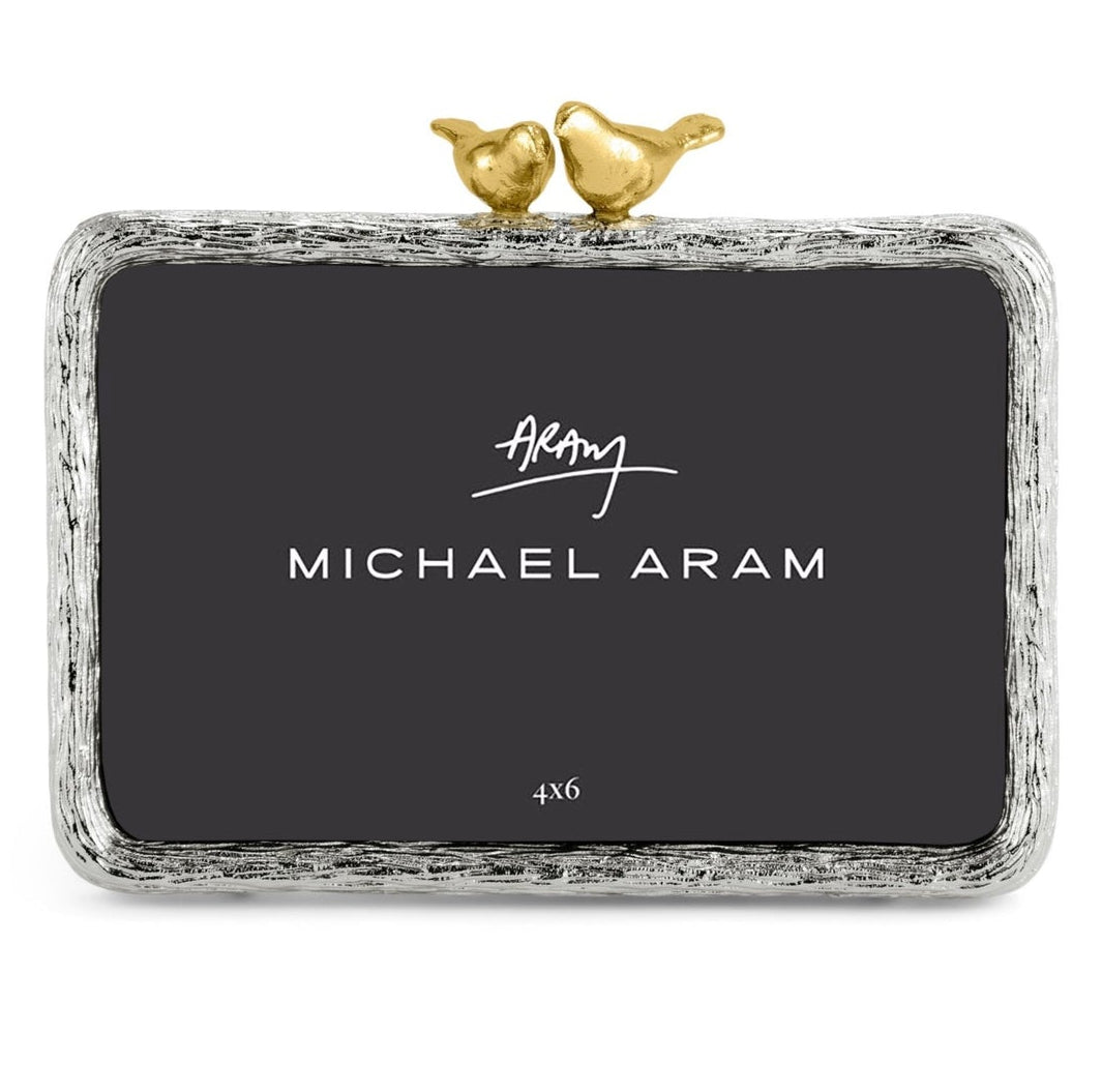 The Michael Aram Lovebirds Frame is a handcrafted rectangular frame with a textured silver border and two gold lovebirds perched on top.