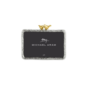 From the Lovebirds Frame Collection by Michael Aram, this elegant rectangular silver picture frame features textured edges and holds a 4x6 photo. Decorated with two small gold bird figurines perched at the top, it makes a thoughtful anniversary or wedding gift—perfect for displaying cherished memories.