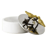 The Michael Aram Lovebirds Trinket Box is a round white box with a lid featuring metallic gold and black leaves and a flower—ideal for storing jewelry elegantly.