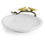 The Lovebirds Trinket Dish by Michael Aram is a white, round jewelry holder inspired by the Tree of Life, featuring a decorative gold branch on the rim with two gold bird figures facing each other.