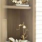 A wooden shelf displays gold and white Michael Aram Orchid Decorative Objects and handcrafted metal sculptures on light bases, with a picture frame partially visible in the background.