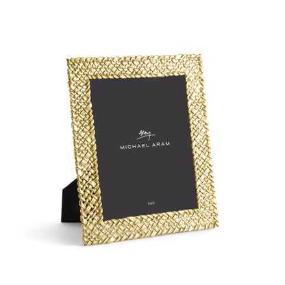A gold woven-pattern photo frame from the Palm Gold Frame Collection by Michael Aram, featuring sculpted textures, a black stand, and a placeholder insert labeled with the brand.