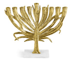 The Michael Aram Gold Palm Menorah, Small features a hand-sculpted tree branch design in antique gold with eight candle holders on a white marble base.
