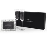 The Michael Aram Reflective Champagne Flute & Heart Frame Gift Set features two flutes and a polished photo frame, elegantly displayed in front of a black Michael Aram box.