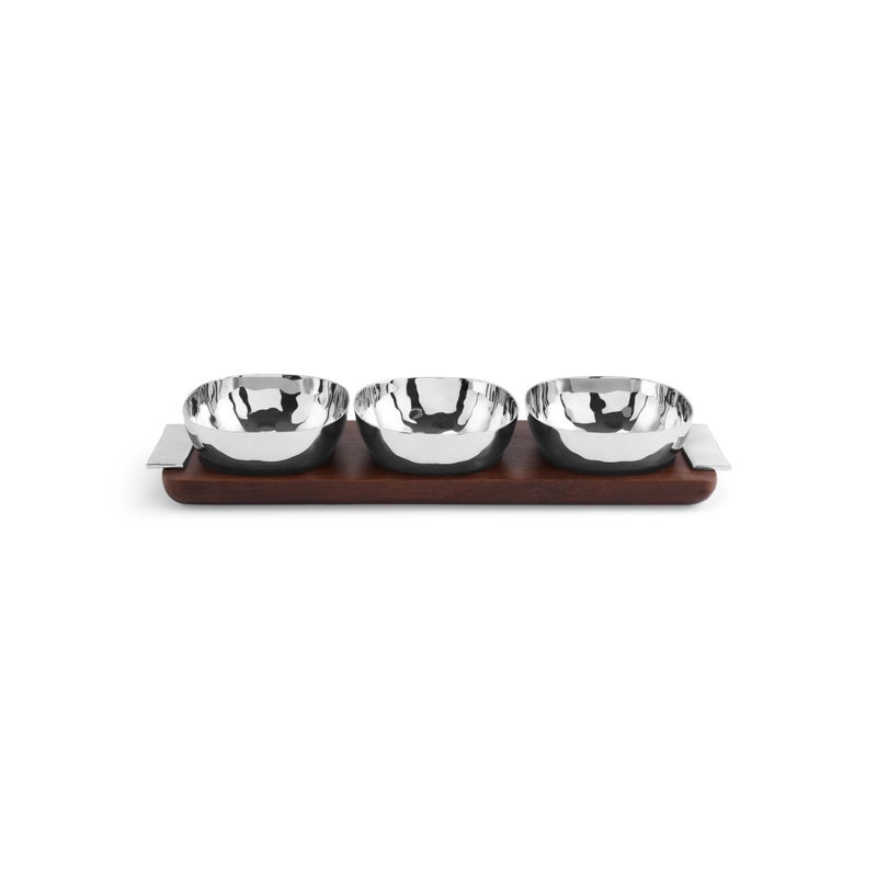 From the Reflective Serveware Collection by Michael Aram, three high-polished stainless steel bowls rest on a rectangular wooden tray with metal handles, creating a modern aesthetic.