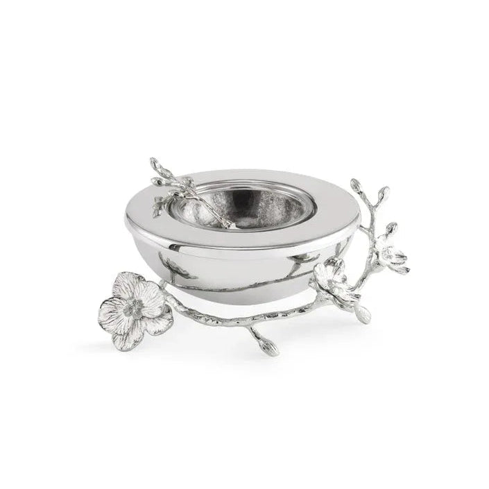 A silver bowl from the Michael Aram Silver Orchid Collection, featuring an attached decorative branch and orchid flower on one side—symbolizing purity and grace—inspired by the orchid plant, displayed against a white background.
