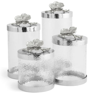 The Michael Aram White Orchid Canister Collection features elegant glass containers adorned with floral accents, highlighting exquisite luxury craftsmanship.