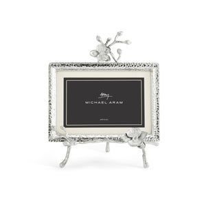 A Michael Aram White Orchid Frame Collection picture frame with textured edges and floral accents displays a card labeled "Michael Aram," evoking the purity and grace of orchids against a white background.
