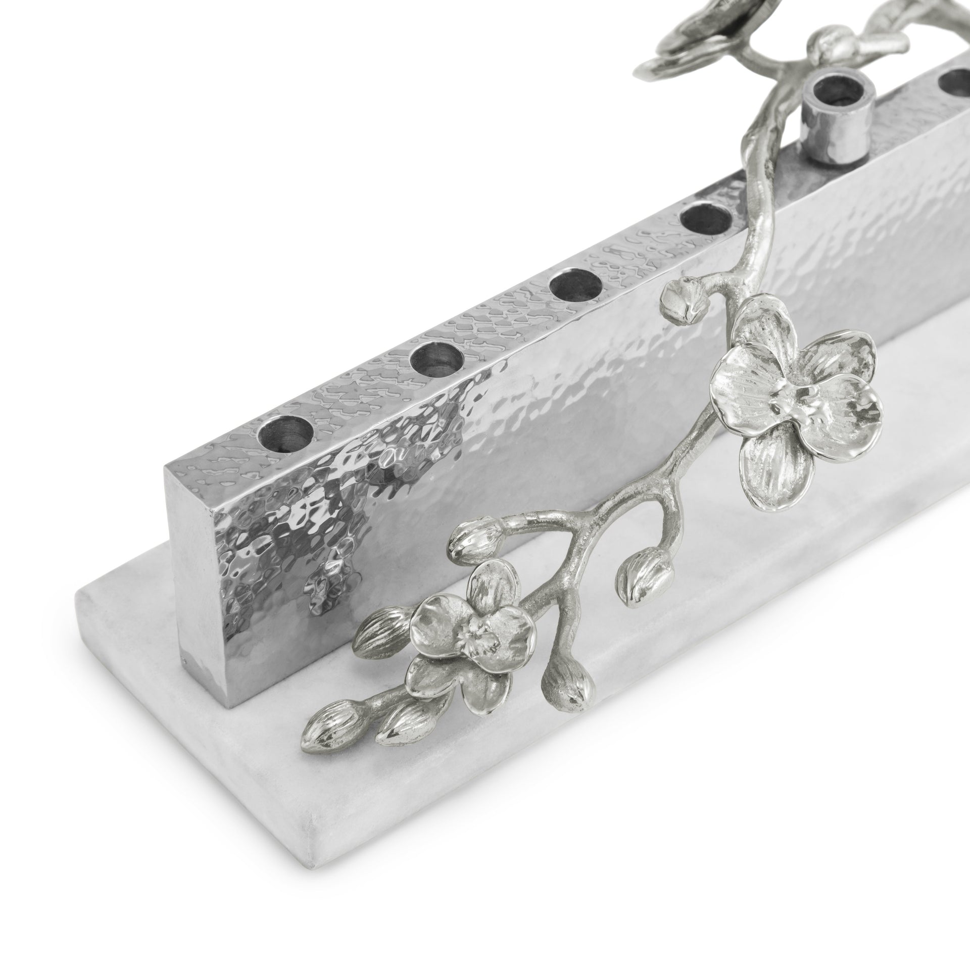 The Michael Aram White Orchid Judaica Collection Menorah features a silver, hammered metal design with floral branch and blossom accents on a white rectangular base.