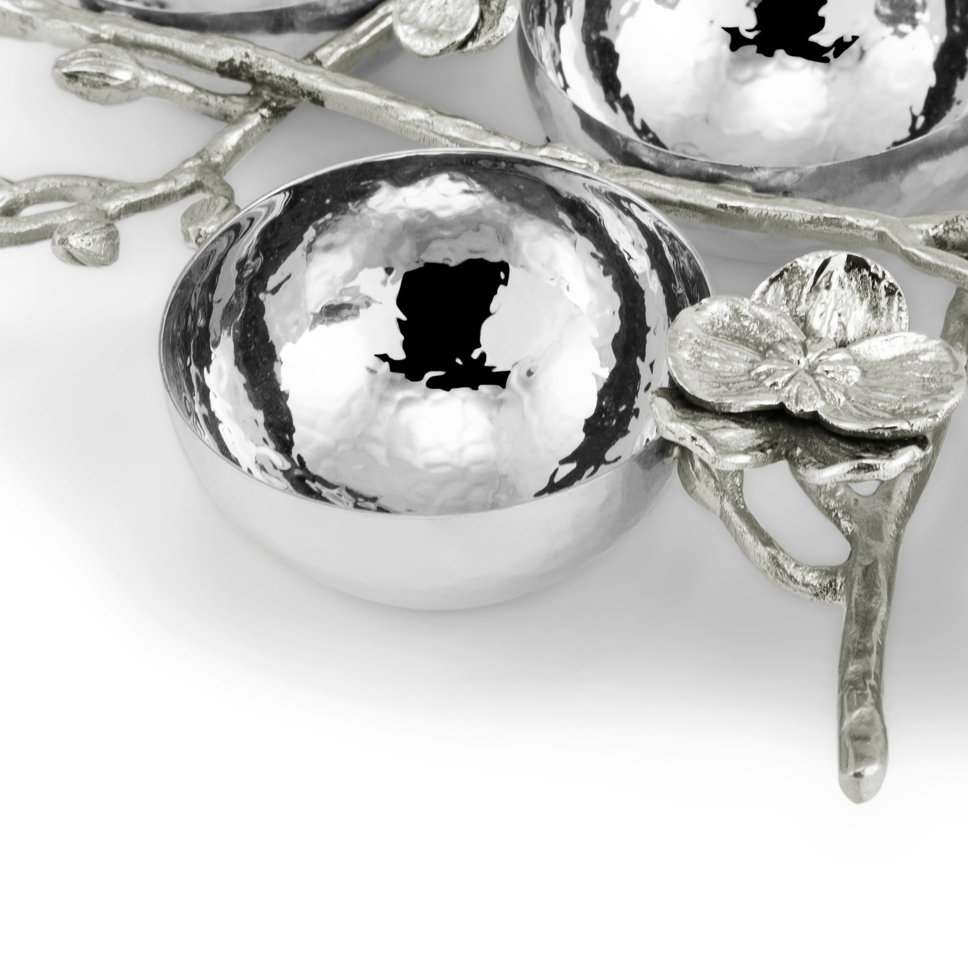 A close-up of a shiny, hammered metal bowl from the Michael Aram White Orchid Judaica Collection, featuring a decorative branch with a flower design against a white background.