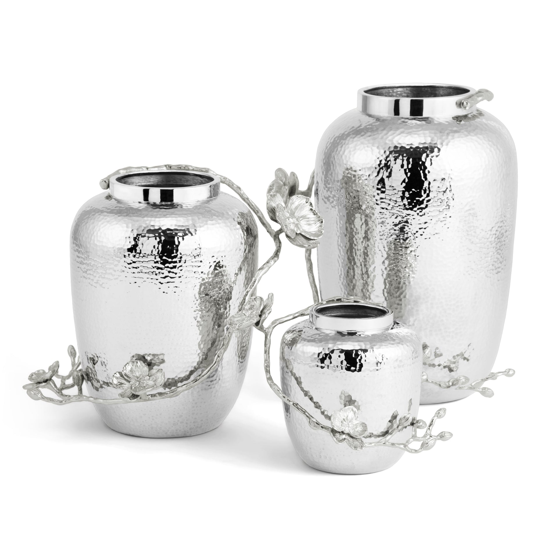 The Michael Aram White Orchid Vase Collection features three silver, hammered metal vases of varying heights, each with a metallic branch and flower motif—striking decorative accents for any space.
