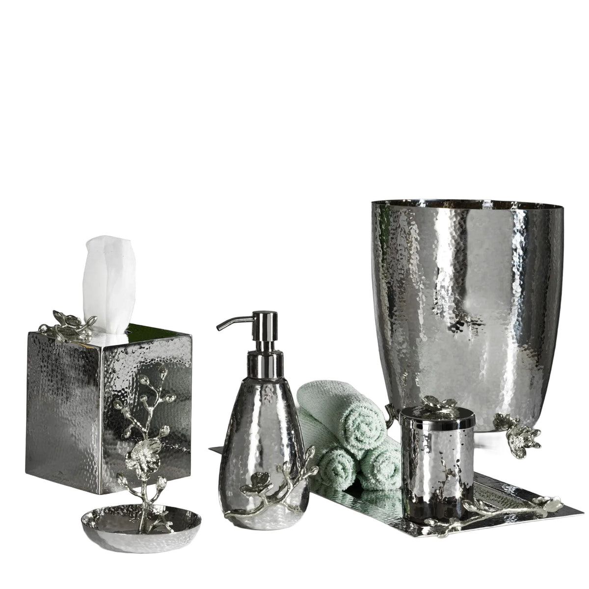 The Michael Aram White Orchid Bath Collection is a six-piece bathroom accessory set featuring a luxurious hammered texture in silver, with elegant pieces including a soap dispenser, tissue box, tumbler, soap dish, waste bin, and rolled green towels.