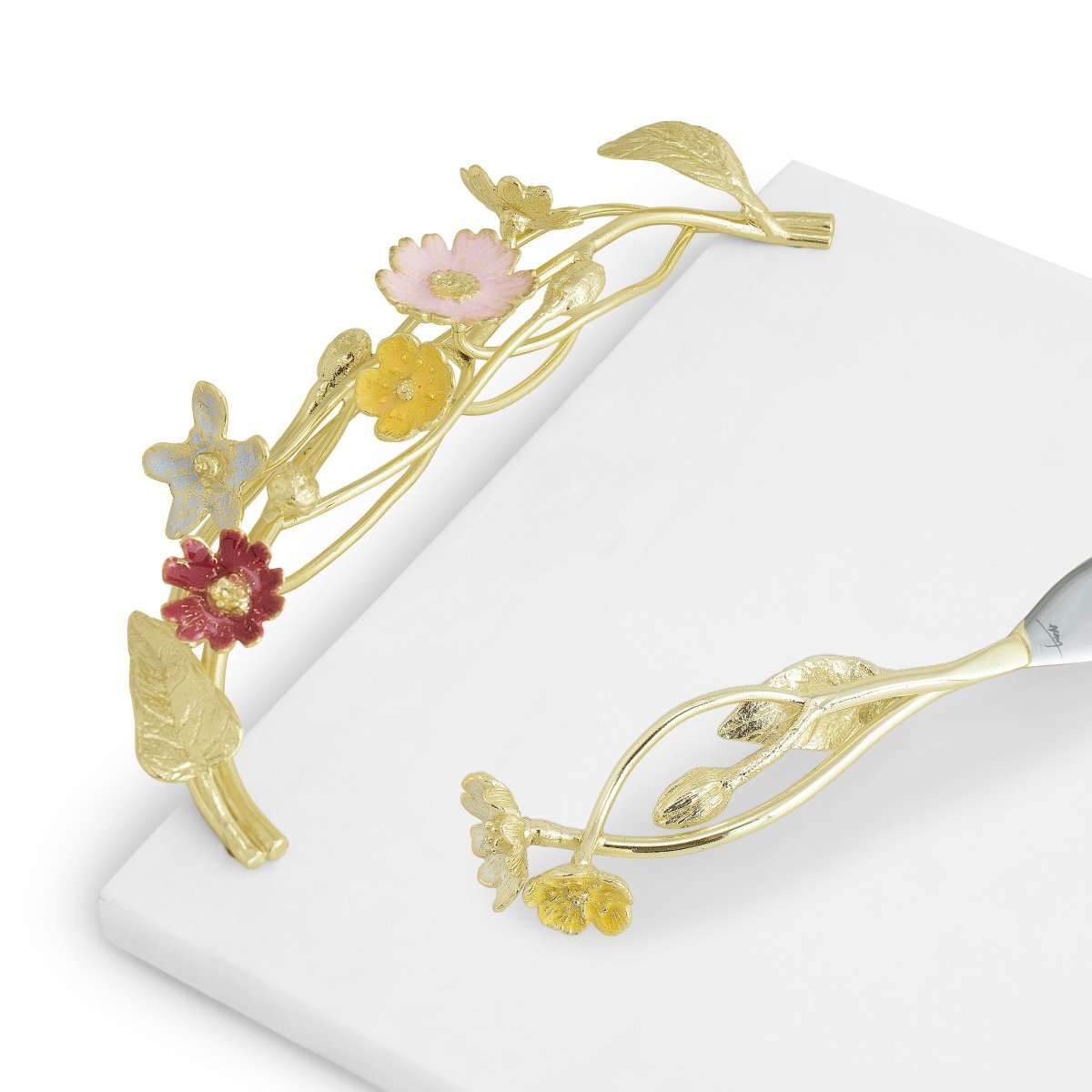 The Michael Aram Wildflower Serveware Collection features a gold cake knife and server set adorned with handcrafted wildflowers, displayed on a white surface.