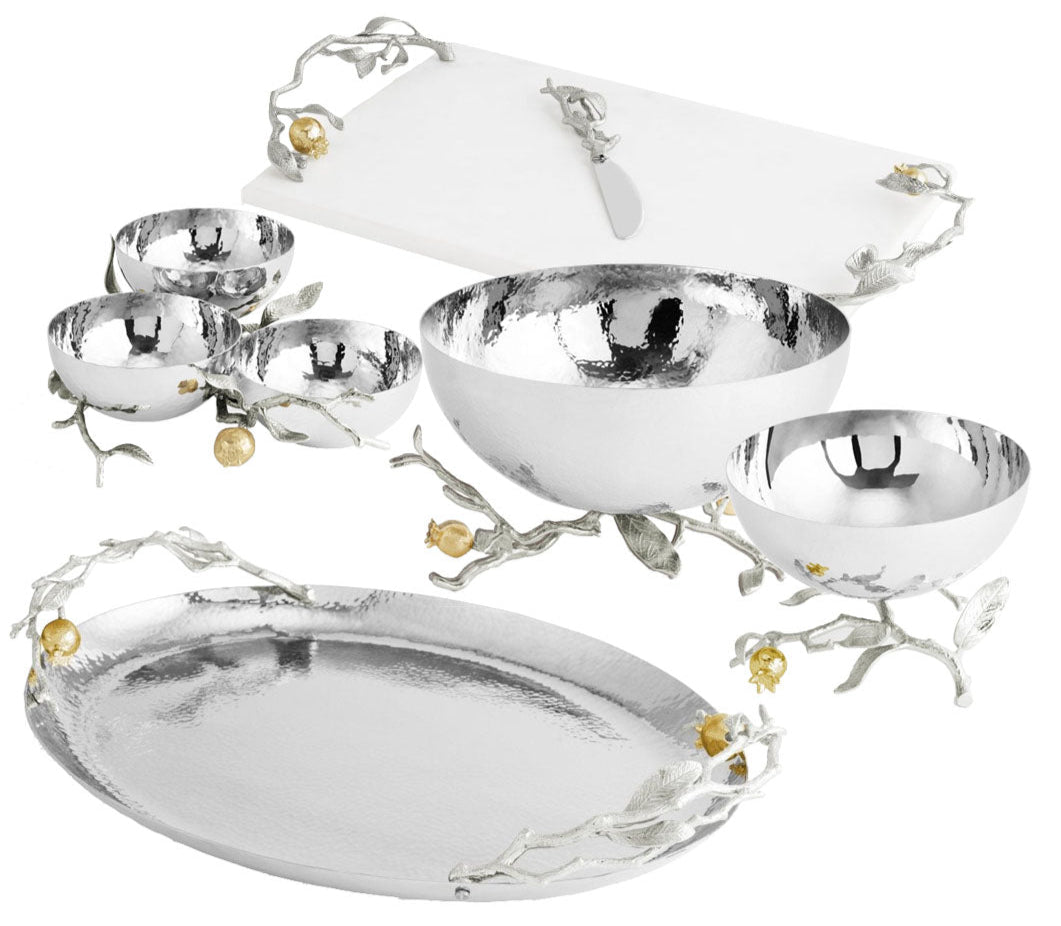 A set from Michael Aram’s Pomegranate Silver & Gold Serveware Collection, featuring silver bowls, a platter, and a cutting board with knife—all adorned with branch and flower accents in stainless steel, nickelplate, and goldplate.