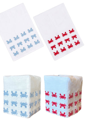 Two white linen cloths from the Haute Home Mini Crab Bath Collection, featuring blue and red crab patterns, are displayed flat and wrapped around square objects on a white background—perfect as an elegant tissue box cover.