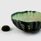 From AE Ceramics’ Sea Urchin Bowl Collection, a handmade green ceramic bowl with a textured, scalloped rim sits beside a sea urchin shell and mossy sphere on a white background.