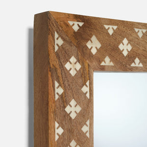Close-up of the Izan Rectangular Mirror by Made Goods, highlighting its wooden frame with geometric cut-out patterns, inlaid white accents, and part of the reflective surface.