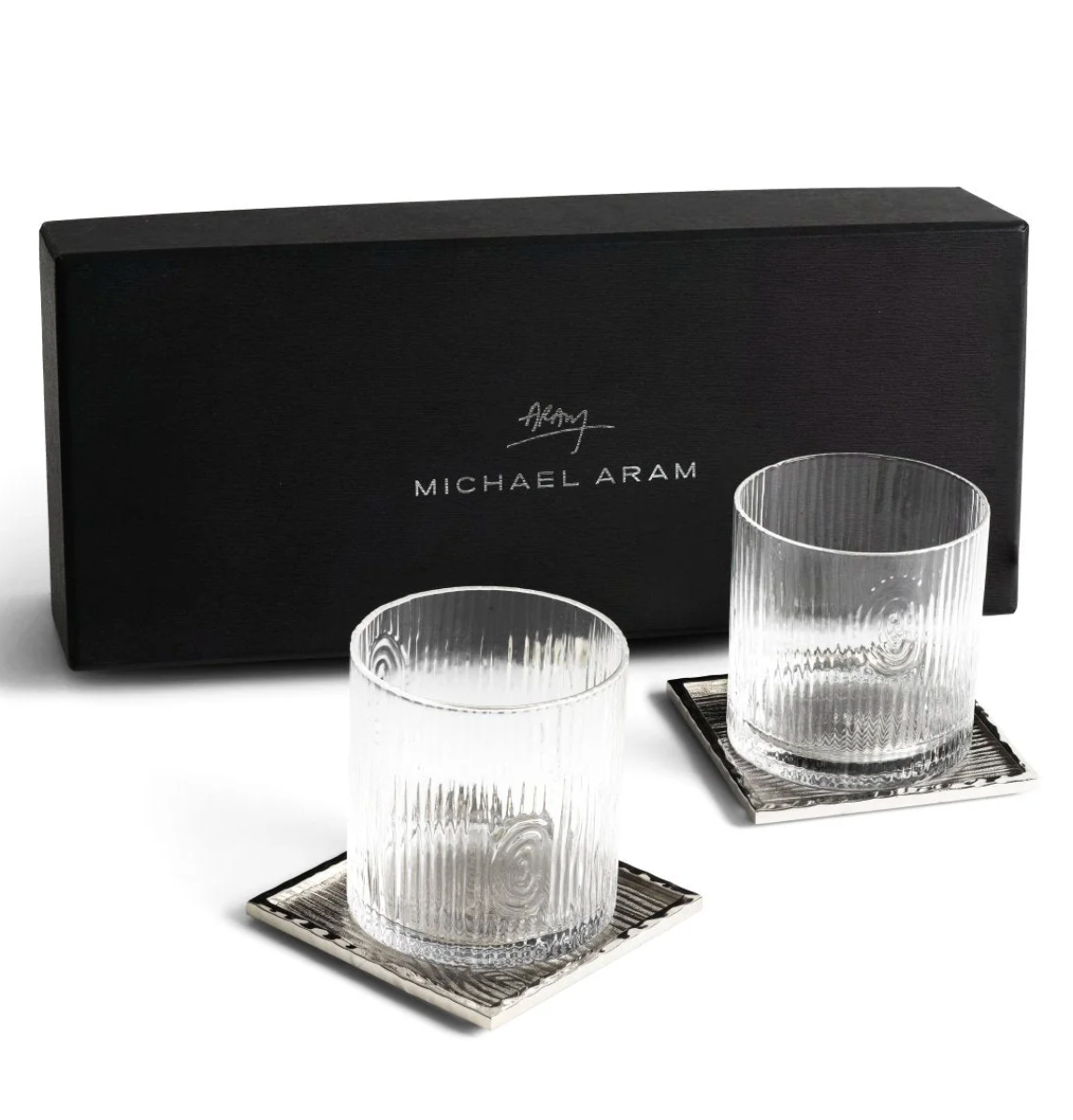 Two ribbed glass tumblers and square silver coasters from the Michael Aram Ivy & Oak Glass and Coaster Gift Set are displayed in front of a black branded box, showcasing rustic elegance.