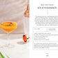 A coupe glass filled with an orange non-alcoholic cocktail from Monday Night Mocktails by Simon & Schuster, garnished with a dried persimmon slice, rests on a white surface alongside a cocktail shaker and green leaves—offering perfect inspiration for those exploring refreshing mocktail recipes.