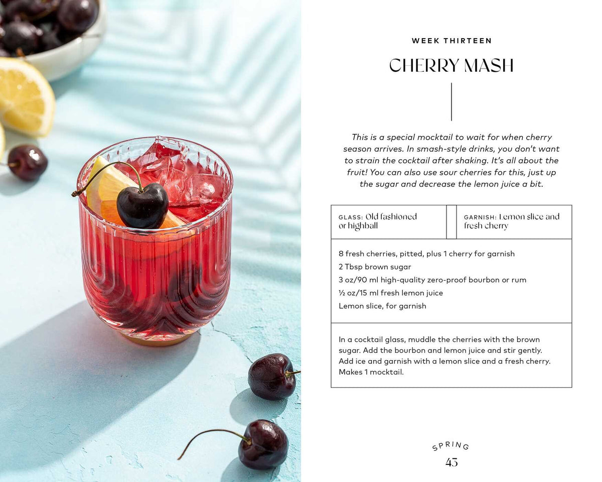 A vibrant red cherry mocktail with ice, topped with a lemon slice and cherry, sits on a table adorned with fresh cherries and lemon wedges. Ideal for fans of delicious non-alcoholic beverages, this enticing drink is featured in Monday Night Mocktails by Simon & Schuster, alongside easy-to-follow mocktail recipes displayed beside the glass.