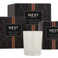 A white Nest Moroccan Amber Candle sits before three black and gold boxes from the Moroccan Amber Candle Collection.