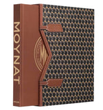 “Moynat” by Assouline is a book with a brown spine and a patterned slipcase, celebrating iconic French luxury leather goods like travel accessories and wardrobe trunks.