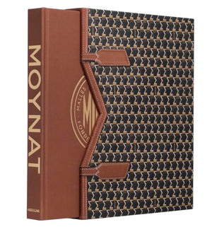 “Moynat” by Assouline is a book with a brown spine and a patterned slipcase, celebrating iconic French luxury leather goods like travel accessories and wardrobe trunks.