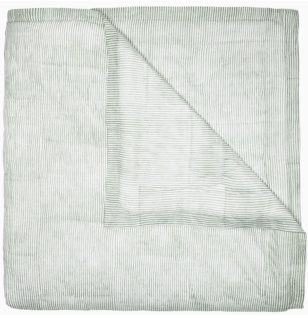 Expertly hand quilted from soft cotton voile, the Nandi Bedding Collection by John Robshaw features a folded light quilt with thin, horizontal green stripes and a corner turned down to reveal an underside with matching stripes, offering a lightweight and luxurious feel.