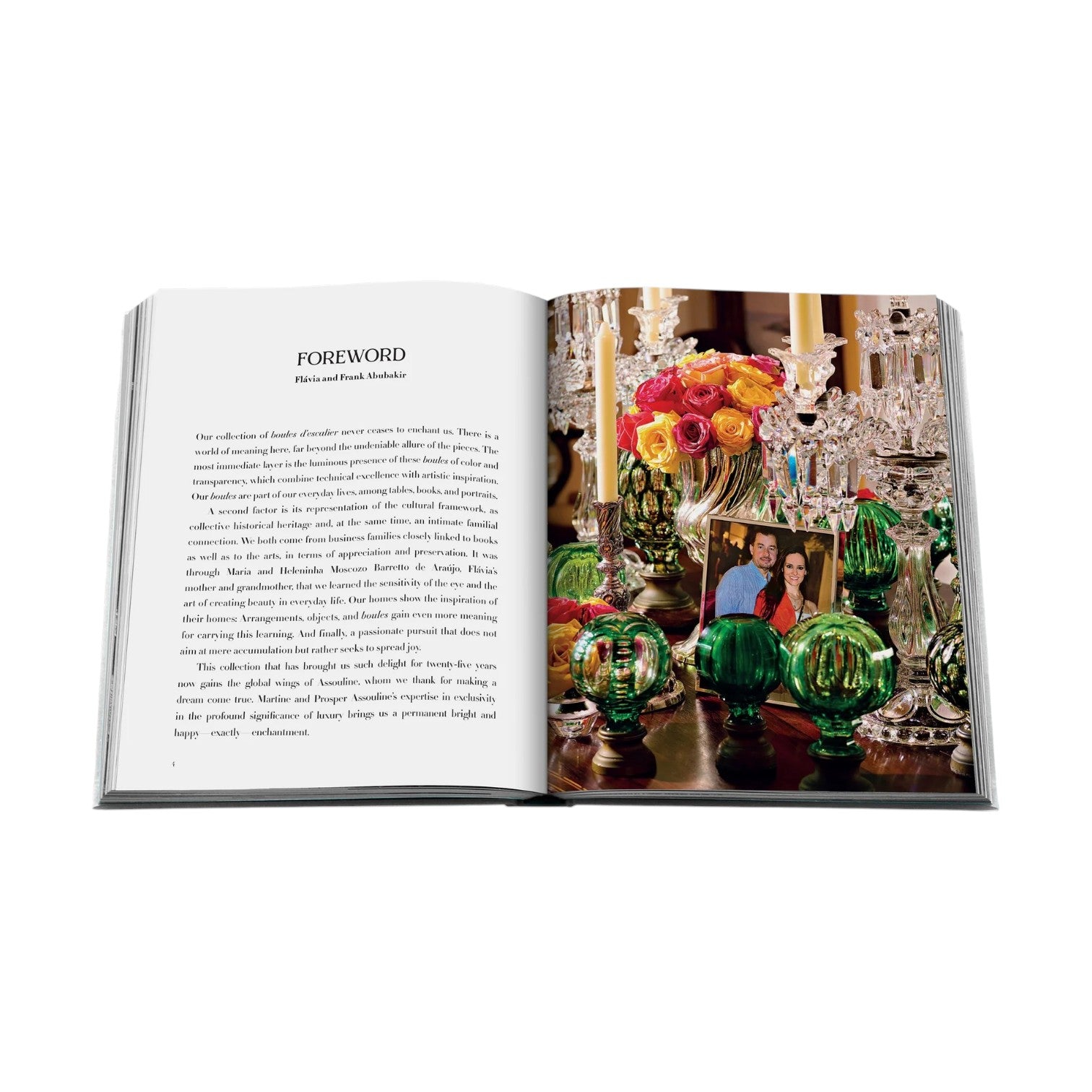 An open book, Boules D'Escalier: The Flávia & Frank Abubakir Collection by Assouline, displays a foreword on the left page and a vibrant image with two people, colorful flowers, green glass decor, and elegant staircase finials on the right.