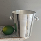 The Hôtel Silver Vintage Ice Bucket with Ball Handles, featuring classic clean lines and a shiny silver finish, sits beside a whole lime, evoking timeless hotel silver serve ware.