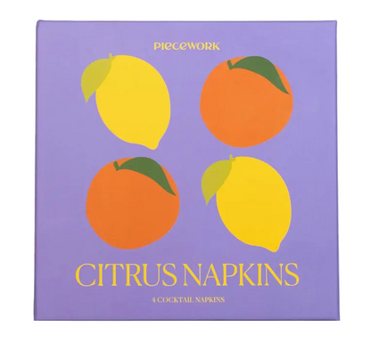 Square purple box of Piecework Citrus Cocktail Napkins featuring illustrations of two lemons and two oranges, labeled “4 COCKTAIL NAPKINS.”